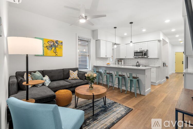 A living room with a grey couch, a blue chair, a round table with a vase of flowers, and a painting on the wall.