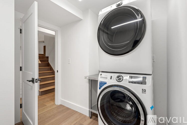 A white washing machine is on top of a white dryer in a white laundry room.