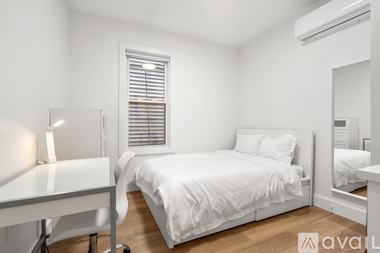 A white bedroom with a bed, desk, and window with blinds.