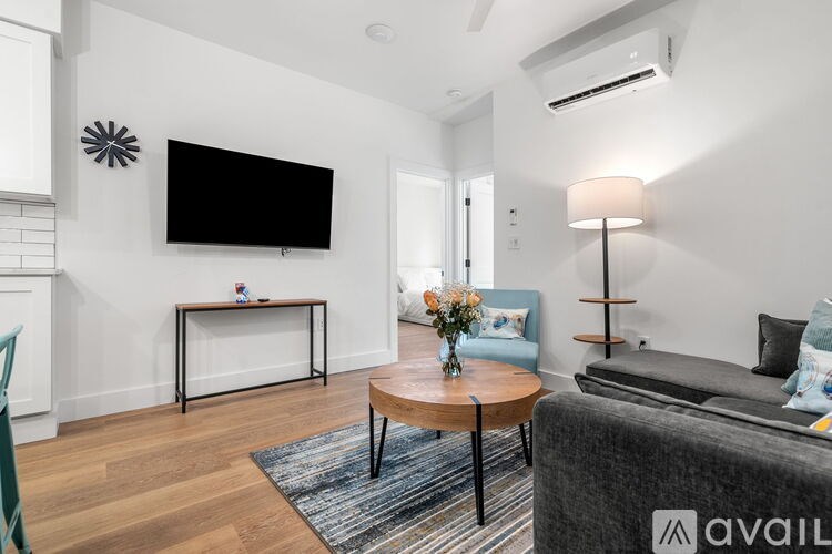 A living room with a grey couch, a coffee table, and a flat screen TV mounted on the wall.