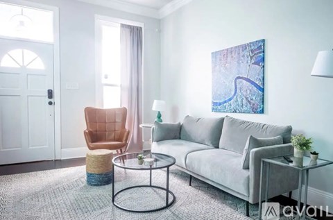 A living room with a grey couch, a brown chair, and a glass table with a plant on it.