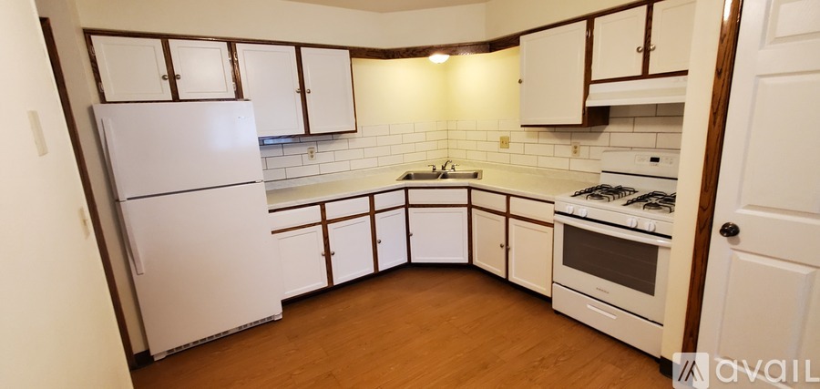 A kitchen with white appliances and wooden floors.