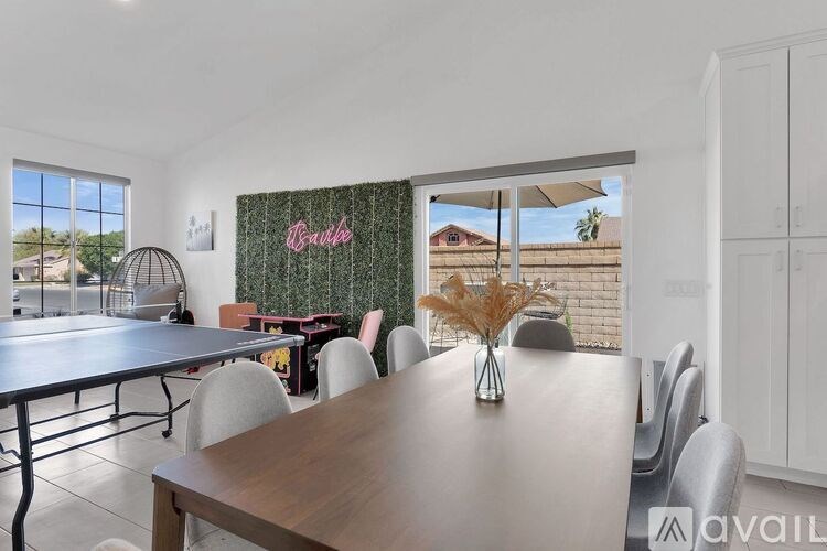 A dining room with a wooden table and chairs, a window with a view of a house, and a green patterned curtain with the word "Boule" written on it.