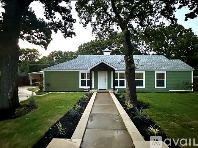 A house with a green exterior and a white door is surrounded by trees.