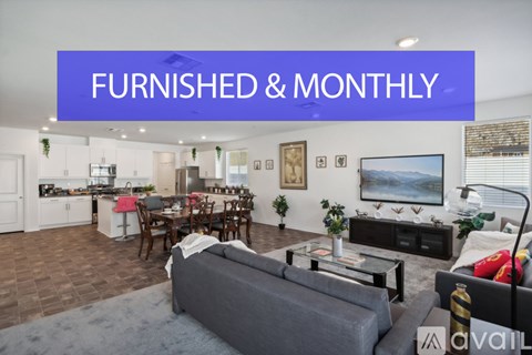 A living room with a grey couch and a kitchen area in the background.
