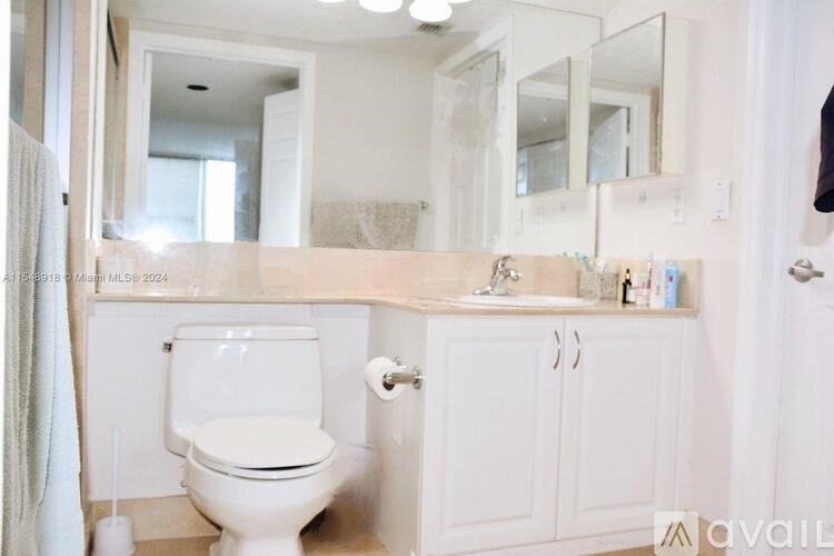 A white toilet is in a bathroom with a white sink and a large mirror.
