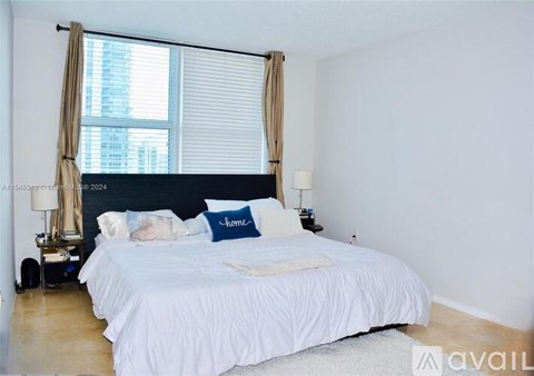 A bedroom with a large bed and a window with curtains.