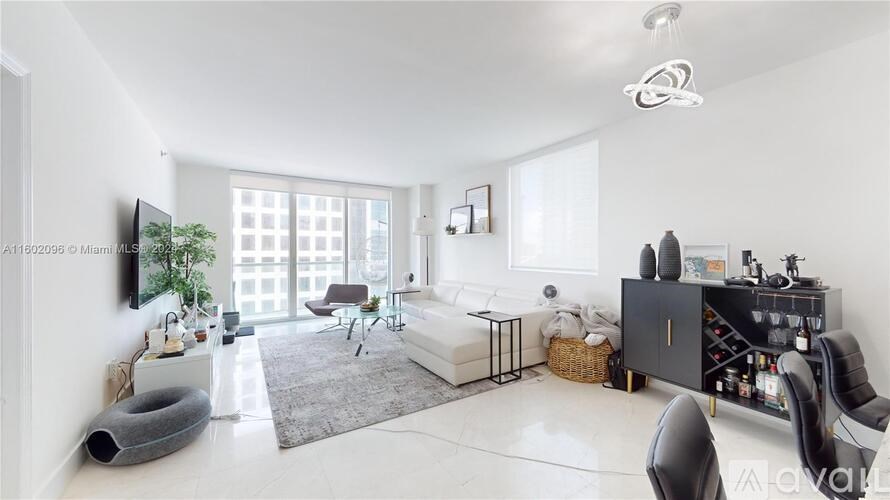 A modern living room with a grey rug, a white sofa, a black cabinet, and a TV on the wall.