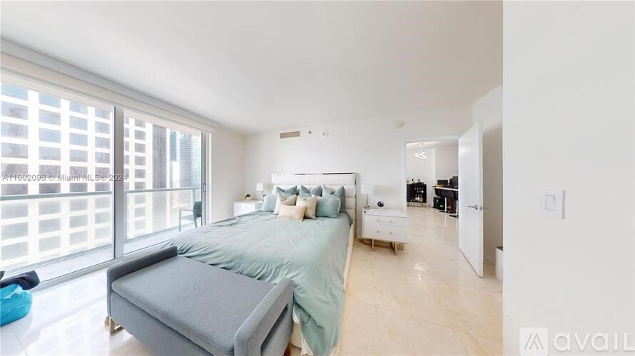 A bedroom with a large bed and a balcony with a view of a cityscape.