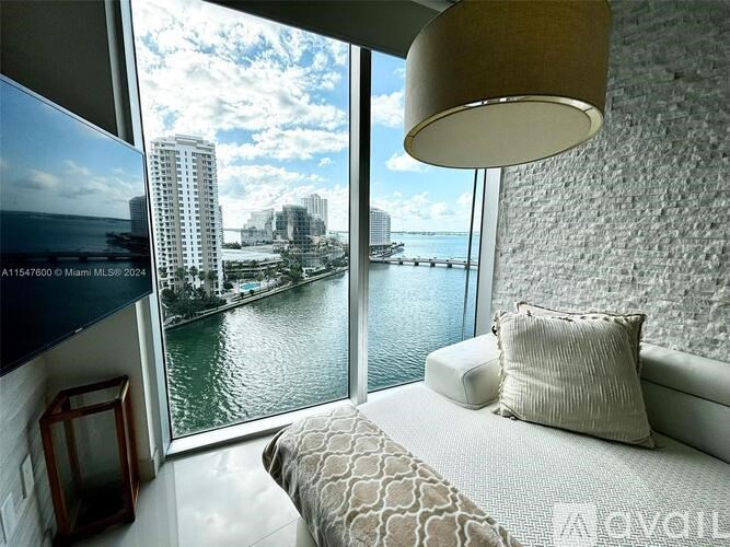 A bedroom with a large bed and a view of the water and buildings outside the window.