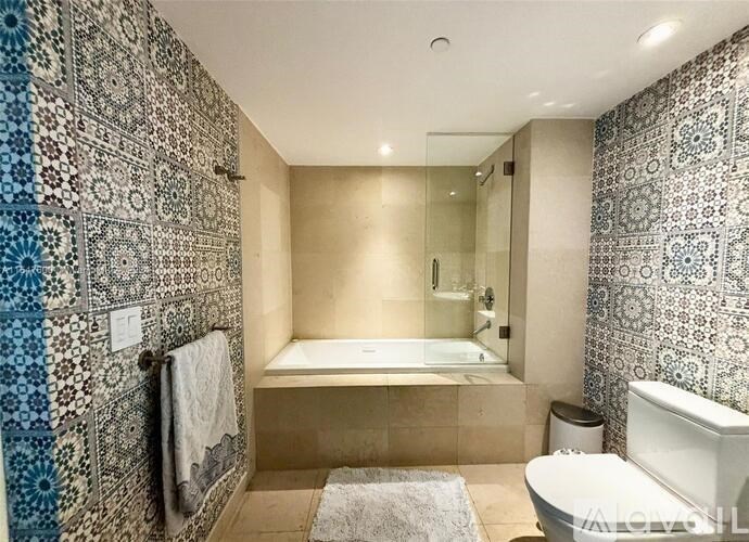 A bathroom with a patterned tile wall and a glass shower door.