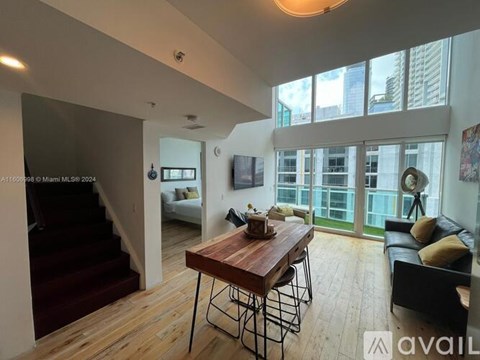 A modern living room with a wooden table and chairs, a couch, and a staircase leading to the upper floor.