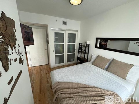 A bedroom with a bed, a mirror, and a wooden floor.
