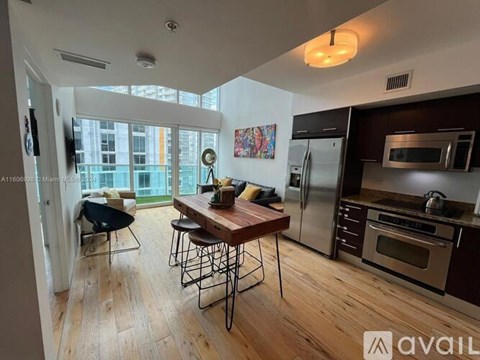 A kitchen with a wooden table and chairs, a refrigerator, a microwave, and a stove top oven.