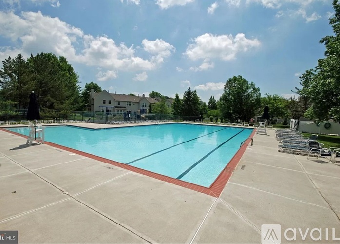 A large outdoor swimming pool surrounded by trees and a building in the background.