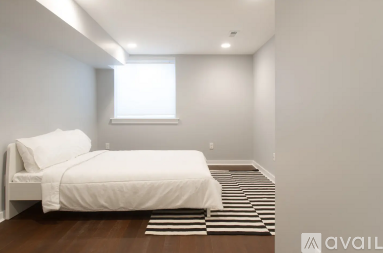A bedroom with a white bed and striped rug.