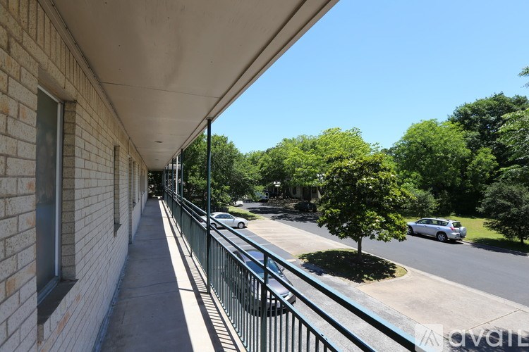 A balcony with a metal railing overlooks a street with cars and trees.