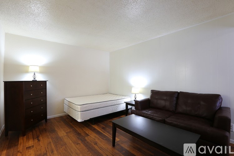 A brown leather couch sits in a room with a white bed and a wooden floor.