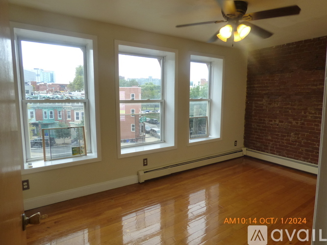 A room with a ceiling fan and three windows overlooking a cityscape.