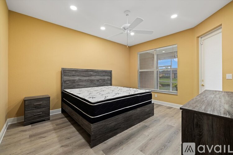 A bedroom with a bed, nightstand, and dresser against a yellow wall.