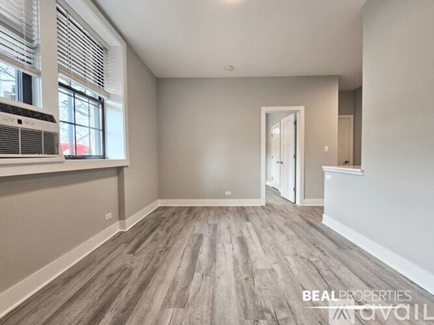 A spacious room with wooden flooring and a large window with blinds.