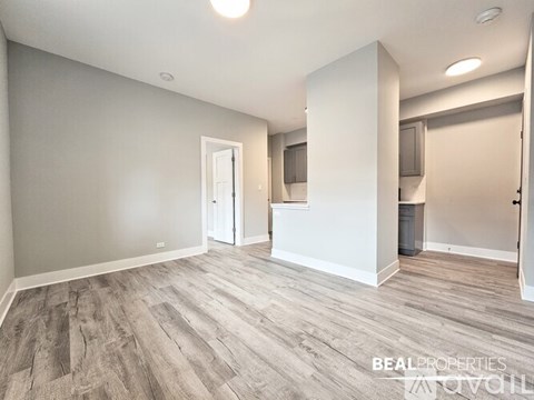 A spacious room with wood flooring and a white column in the middle.