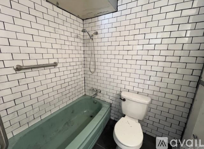 A white toilet is next to a green bathtub in a bathroom with white tiled walls.