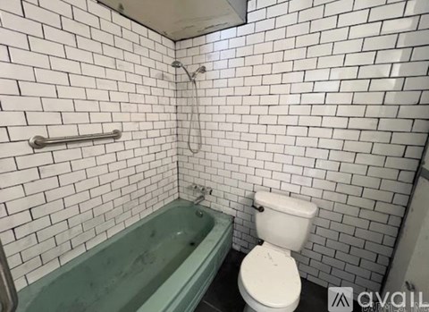 A white toilet is next to a green bathtub in a bathroom with white tiled walls.