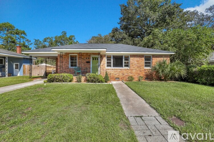 A house with a brick facade and a green door is surrounded by a well-kept lawn.