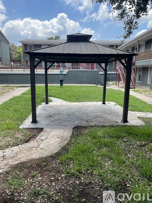 A gazebo with a black roof is situated in a grassy area with a concrete walkway leading to it.