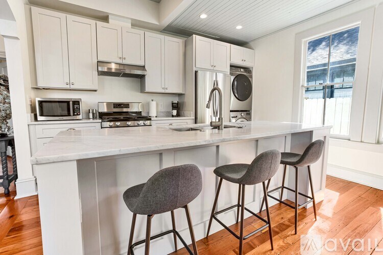 A kitchen with white cabinets and a white countertop with two grey barstools.