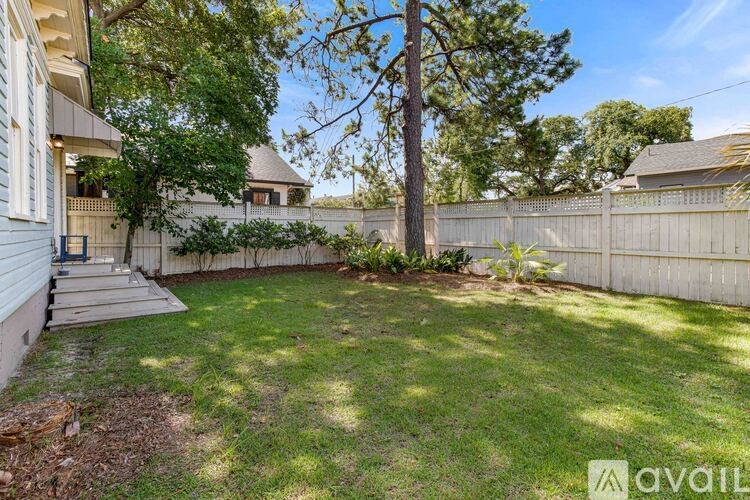 A backyard with a tree, a fence, and a house.
