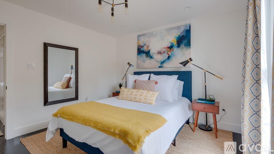 A bedroom with a bed covered in a yellow blanket and a painting on the wall.
