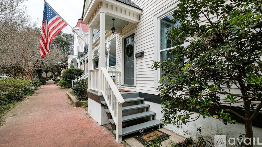 A white house with a red brick walkway and an American flag.