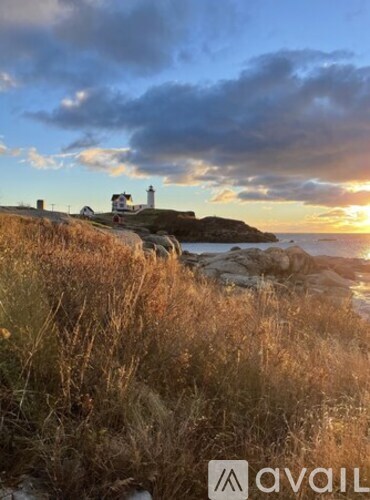 A lighthouse stands on a cliff overlooking the sea at sunset.