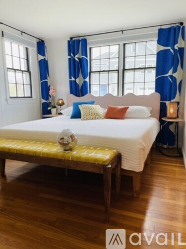 A bedroom with a bed, a bench, and a window with blue curtains.