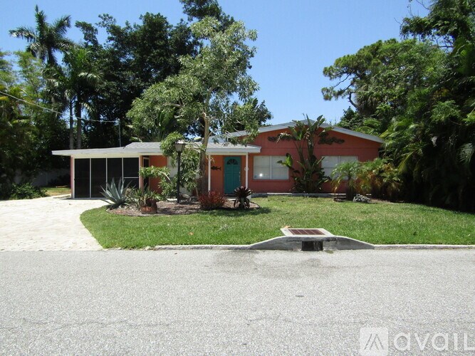 A house with a red door and a green window is surrounded by trees.