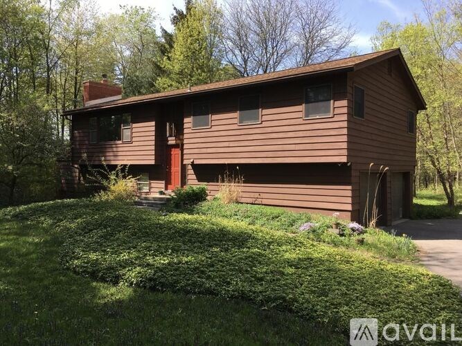 A brown house with a red door is surrounded by greenery.