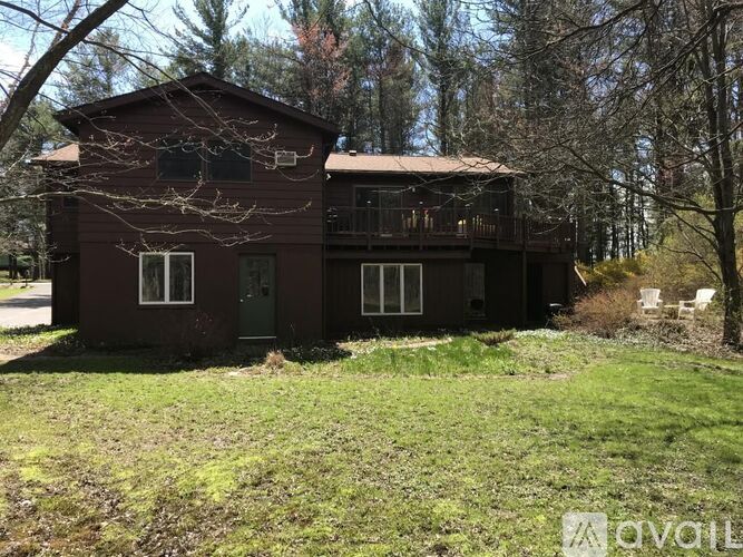 A brown house with a balcony and a green door is surrounded by trees.
