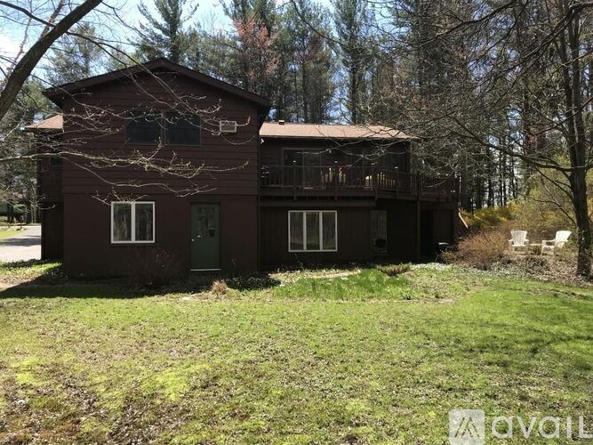 A brown house with a balcony and a green door is surrounded by trees.