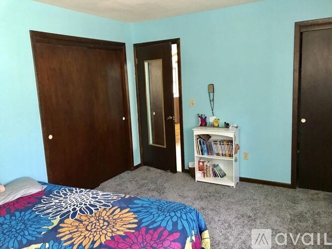 A bedroom with a bed, a bookshelf, and two doors.