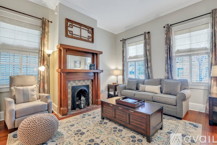 A living room with a fireplace, a grey sofa, a wooden coffee table, and a patterned rug.