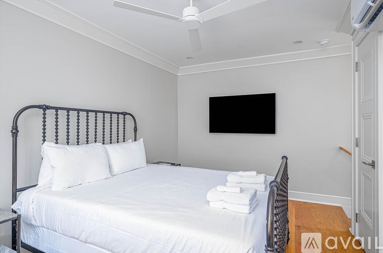A bedroom with a bed, pillows, a chair, and a television mounted on the wall.