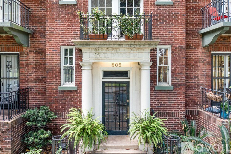 A red brick building with a black door and a balcony with plants.
