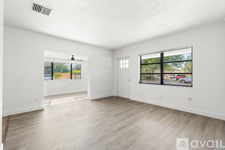 A spacious room with wooden flooring and two windows.