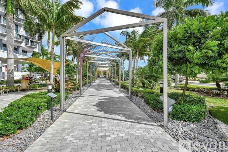 A walkway with a metal frame and a yellow canopy leads through a tropical garden.