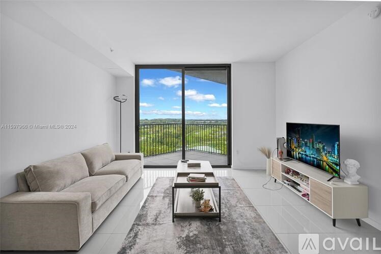 A living room with a large window overlooking a fence and a flat screen TV on a white stand.