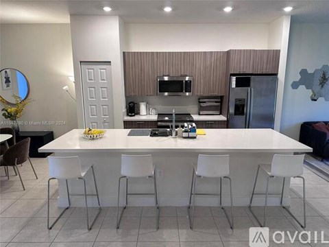 A modern kitchen with a white island and white chairs.