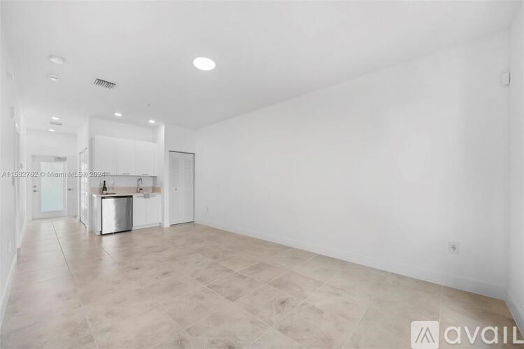 A spacious, empty room with a kitchenette in the distance.