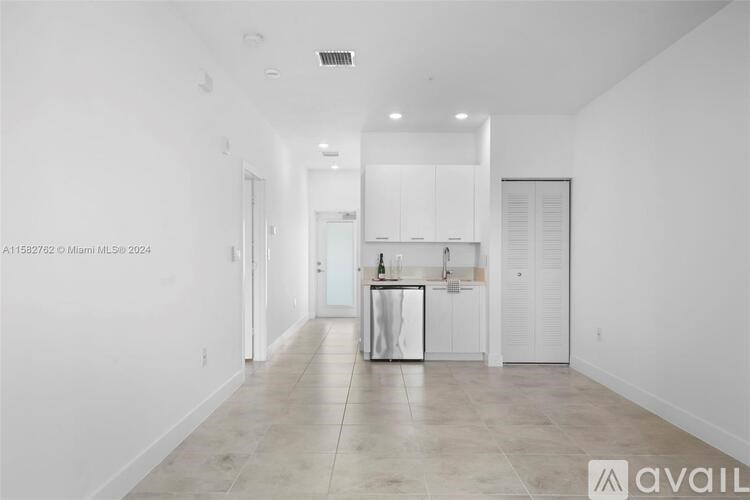 A spacious, empty room with a kitchen area in the background.